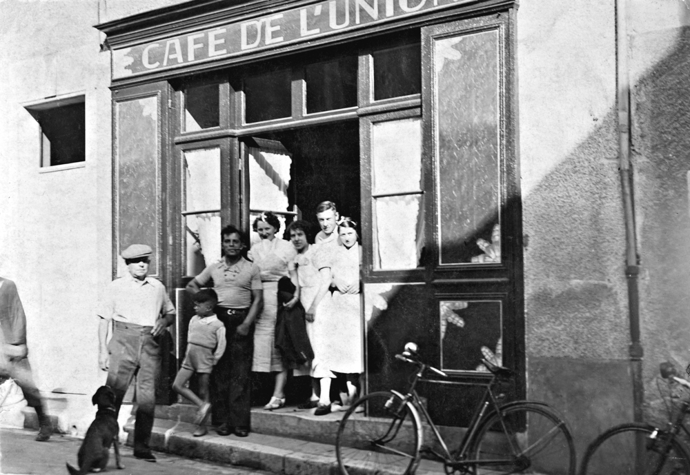 De gauche à droite, avec d’autres personnes, Raymond (casquette blanche), Paul (fumant la pipe) et Raymonde (au centre de la porte), à l’entrée du Café de l’Union. © Fabien Jaffredo.