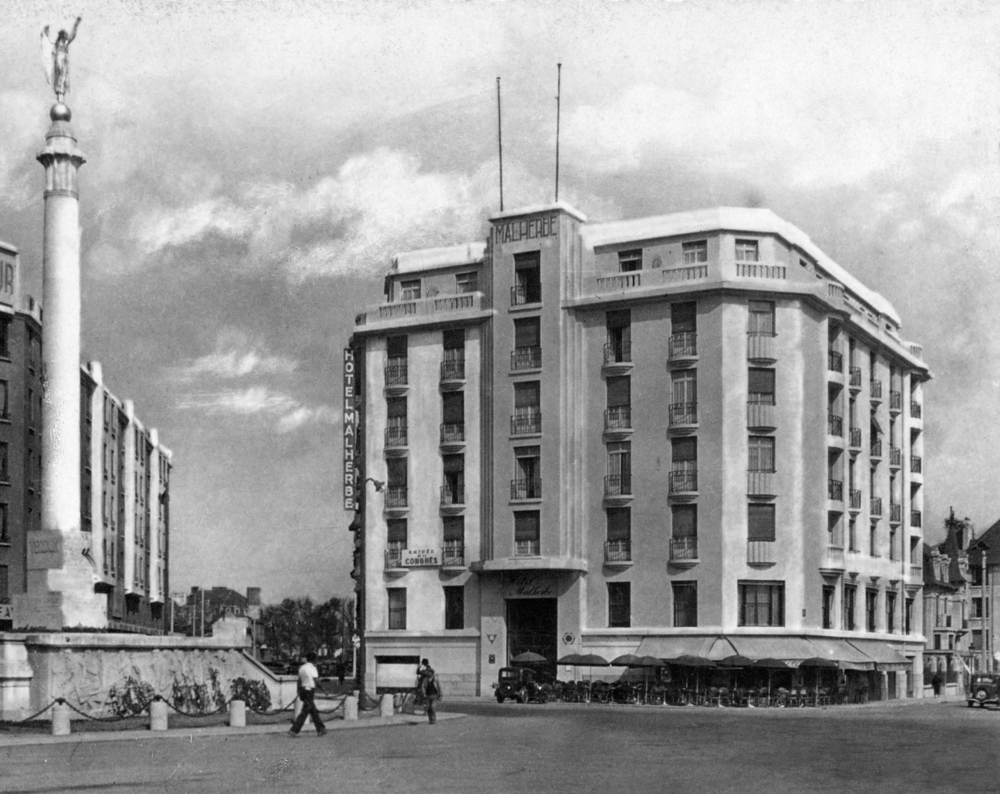 L’hôtel Malherbe avant guerre ; à gauche, le monument aux morts. Carte postale, collection Mémoire Vive.